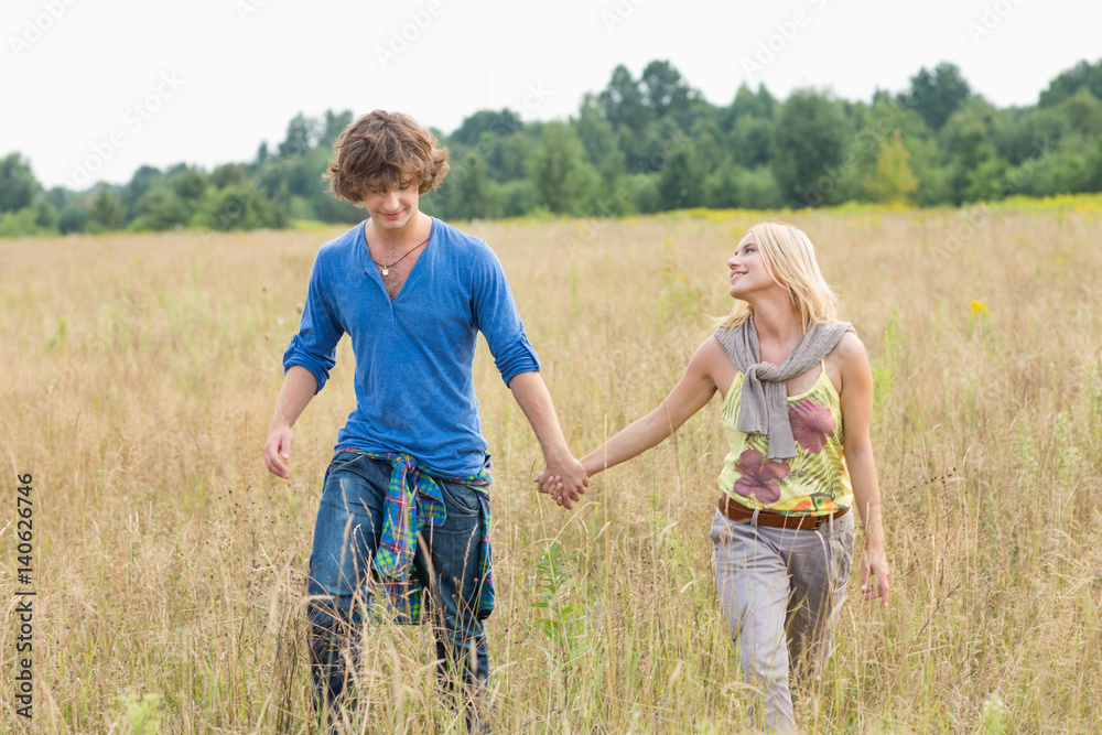 Young couple holding hands while walking through field Young couple holding hands while walking through field