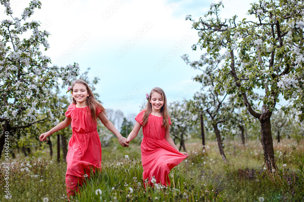 Twin sisters playing in blooming fruit garden. Cute little girls with bunch of dandelions near apple trees in blossom. Kid enjoying happy childhood. Family, love, peace and happiness concept