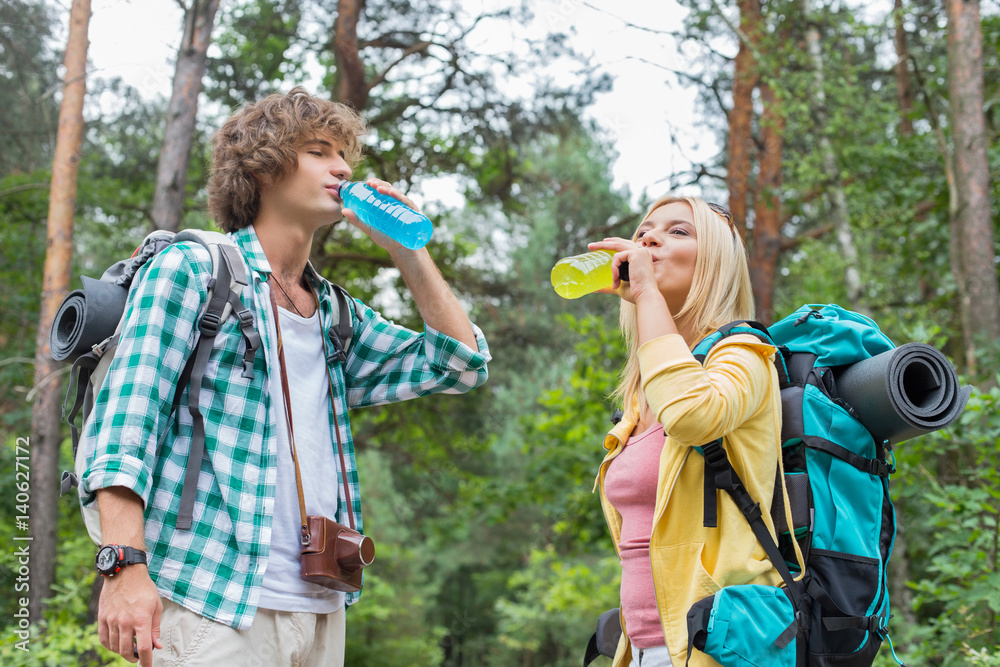 Fototapeta premium Young hiking couple drinking energy drinks in forest
