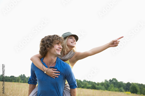 Happy woman showing something while enjoying piggyback ride on man in field