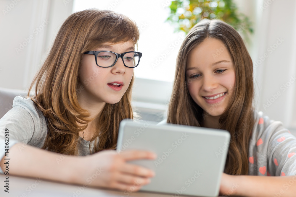 Sisters using digital tablet at table in house Sisters using digital tablet at table in house
