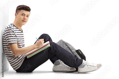 Teenage student leaning against a wall writing in a notebook photo
