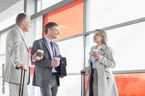 Businesspeople with coffee cups talking on railroad platform