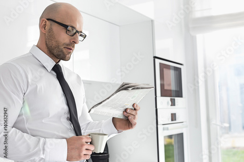 Mid adult businessman having coffee while reading newspaper at home