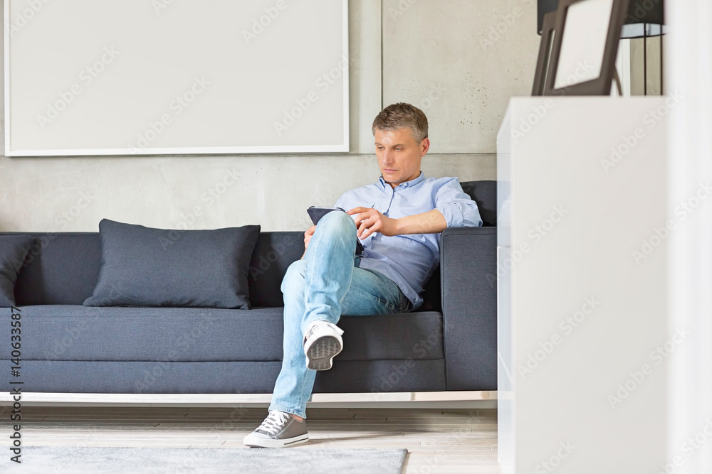 Full-length of Middle-aged man using digital tablet on sofa Full-length of Middle-aged man using digital tablet on sofa