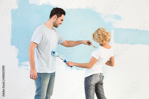 Playful couple painting each other in new house