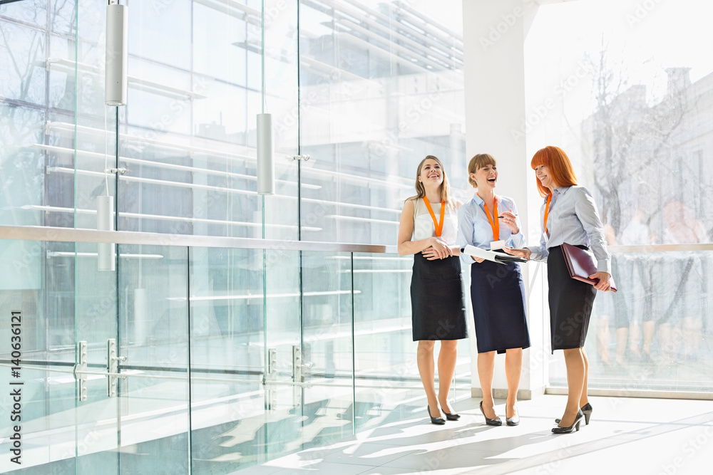 Happy businesswomen standing against glass wall in office