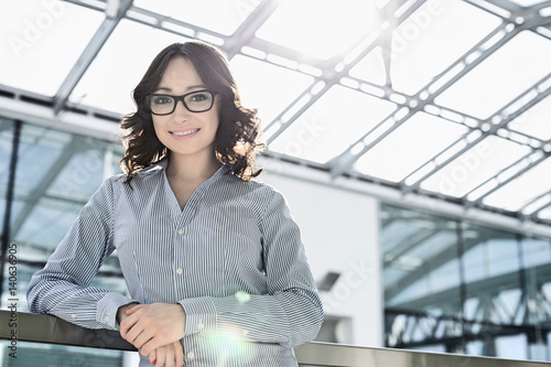 Portrait of happy young businesswoman leaning on railing in office