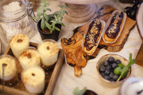 Eclairs with chocolate and wulnut on wooden tray. Sweet bar in area of wedding party
