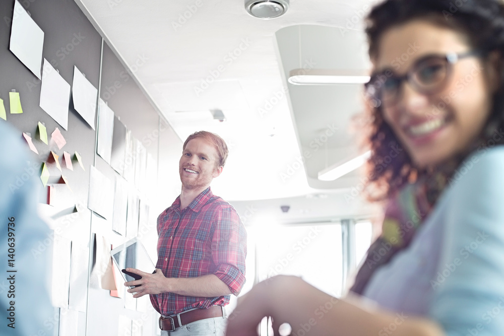 Smiling businessman with female colleague in foreground at creative office Smiling businessman with female colleague in foreground at creative office
