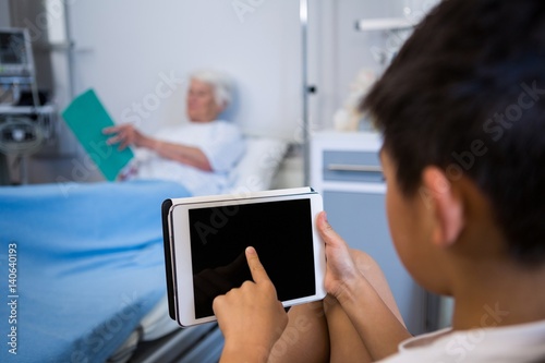 Boy using tablet while senior patient reading a book