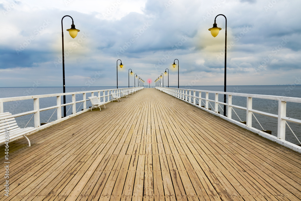 Symmetrical wooden pier with lanterns with dramatic sky.