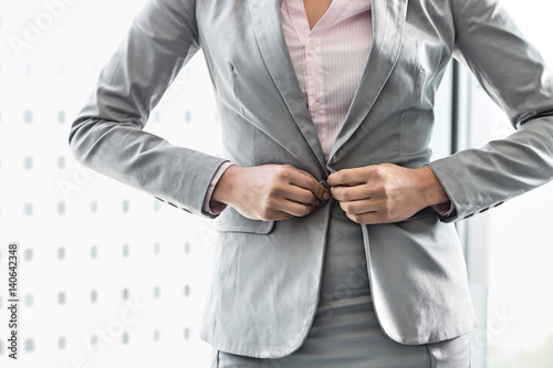 Midsection of businesswoman buttoning her blazer