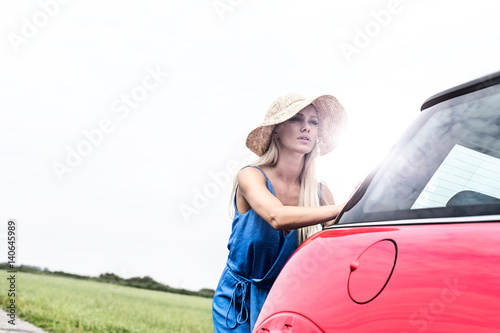 Woman pushing broken down car against clear sky © moodboard
