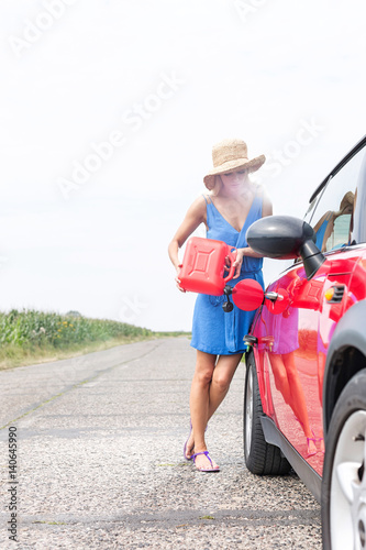 Full-length of woman refueling car on country road against clear sky