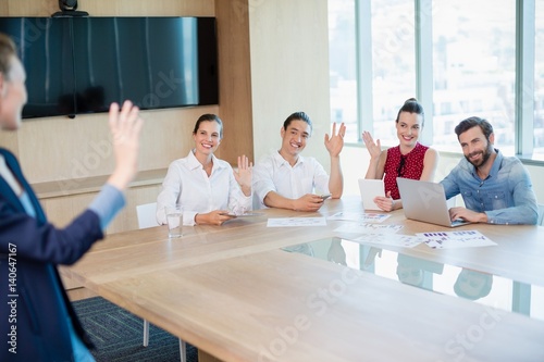 Business executives waving hands to colleague in conference room