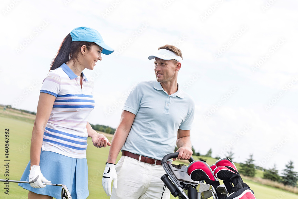 Happy man and woman conversing at golf course against clear sky