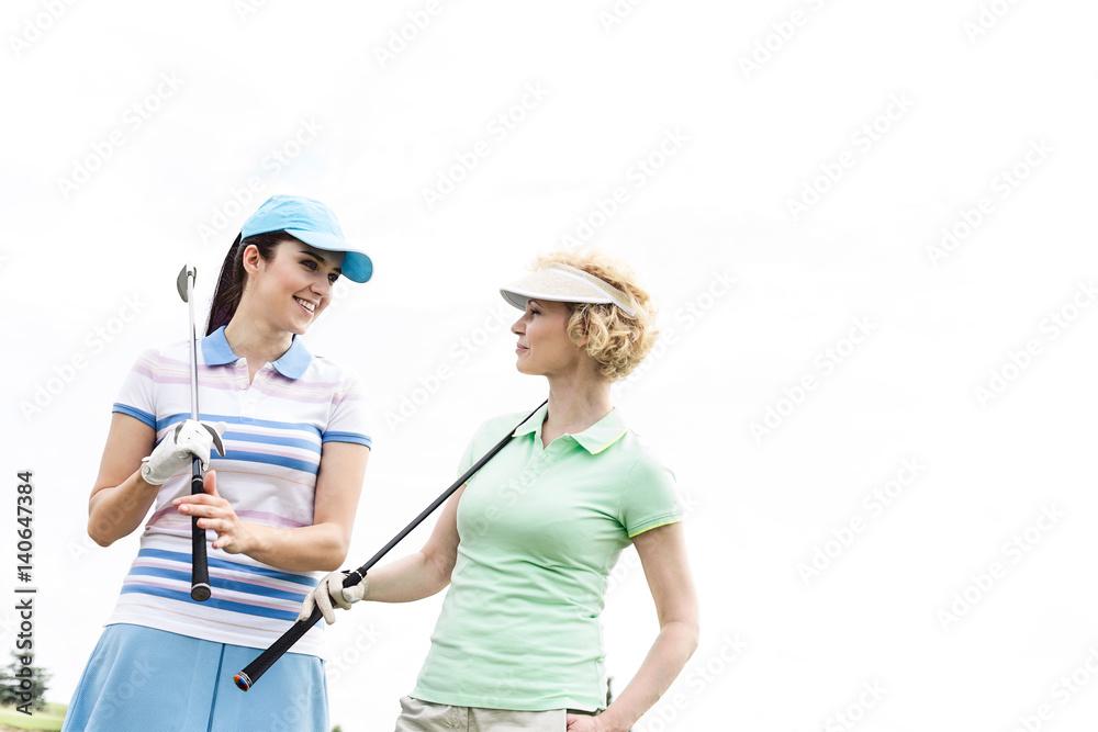 Happy female golfers looking at each other against clear sky Happy female golfers looking at each other against clear sky
