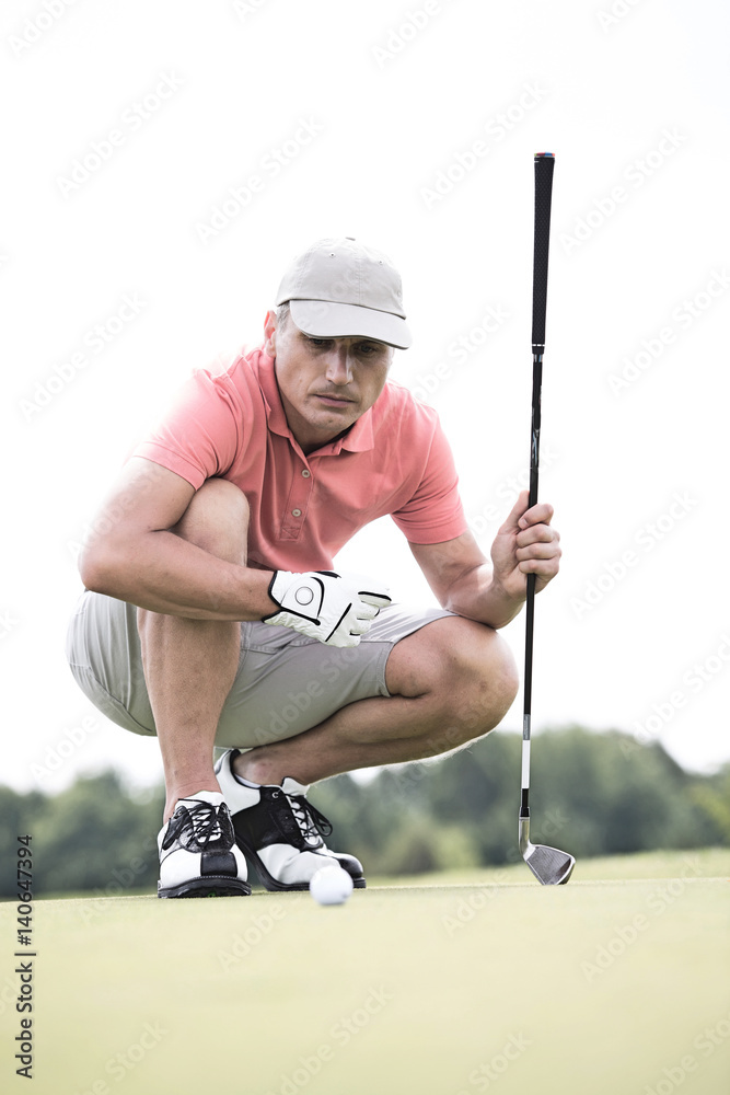 Obraz premium Middle-aged man aiming ball while crouching on golf course