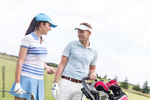 Happy man and woman conversing at golf course against clear sky