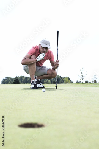 Middle-aged man looking at ball while crouching on golf course