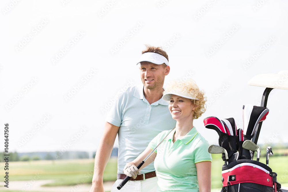 Smiling golfers standing at golf course against clear sky