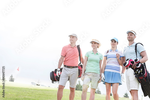Male and female friends standing at golf course against clear sky
