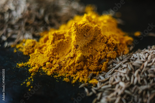 Turmeric powder spice on black, surrounded by other spices.