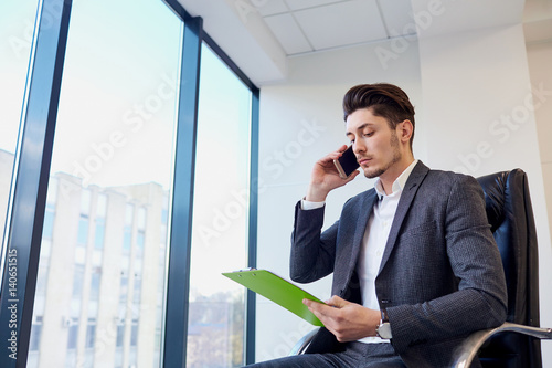 Businessman with documents hands of talking on a cell in modern office.