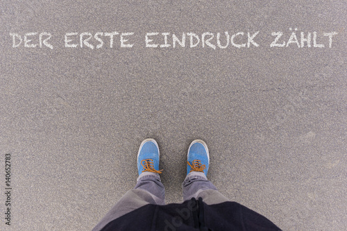 Der erste Eindruck zaehlt, German text for First Impressions Count text on asphalt ground, feet and shoes on floor photo