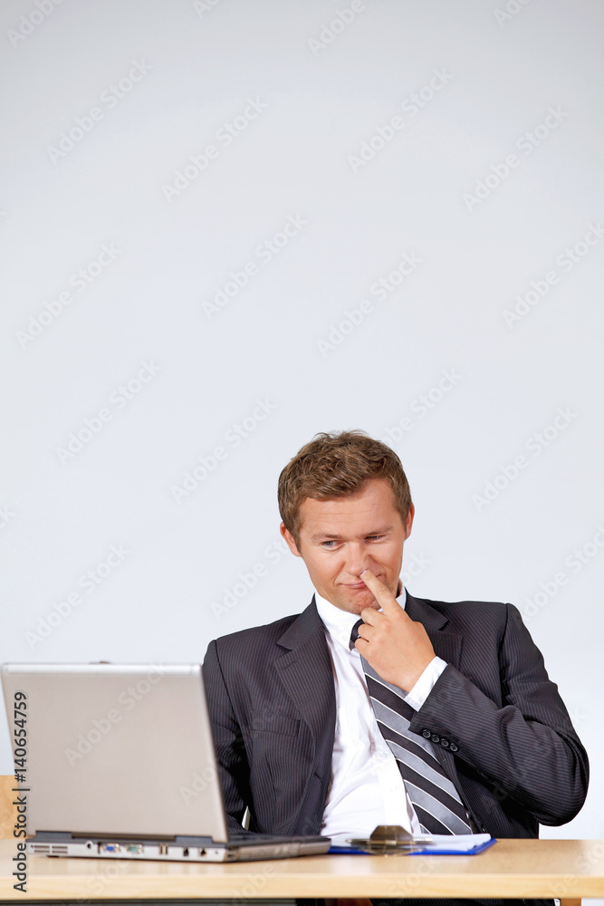Businessman picking nose, looking at laptop in office Businessman picking nose, looking at laptop in office