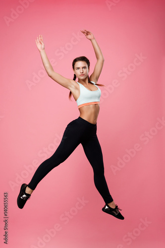 Pretty sporty woman in top and leggins jumping as ballerina
