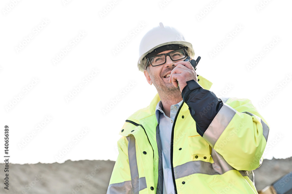 Happy supervisor using walkie-talkie at construction site against clear sky Happy supervisor using walkie-talkie at construction site against clear sky
