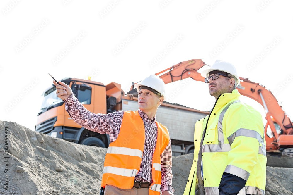 Engineer showing something to colleague while discussing at construction site against clear sky Engineer showing something to colleague while discussing at construction site against clear sky