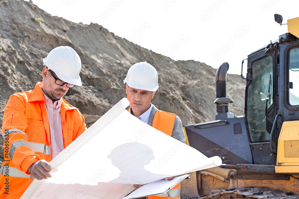 Engineers analyzing blueprint at construction site Engineers analyzing blueprint at construction site