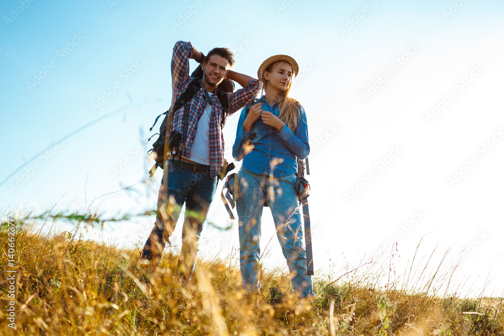 Young couple of travelers with backpacks smiling, standing in field.