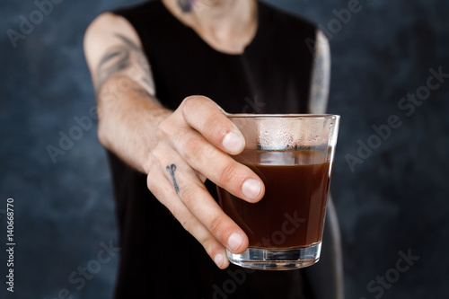 Male barista stretching glass with coffee to camera.