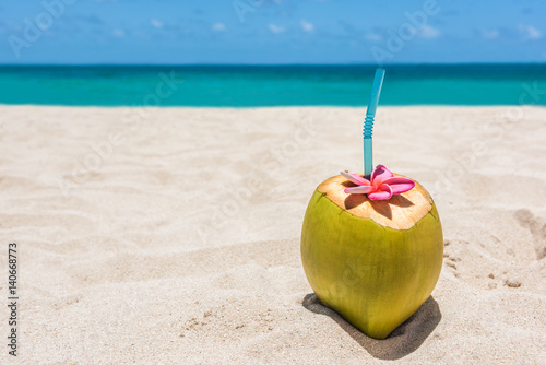 Fresh young coconut lying on the sand beach background with straw ready for drink. Tropical vacation travel concept. Copy space. White sandy destination