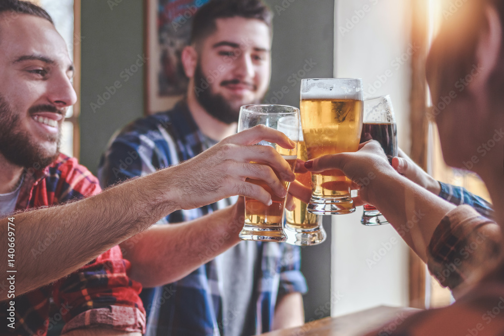 Hipster Friends cheering with beer glasses sitting around cafe bar table
