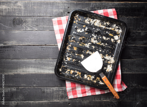 Metal baking tray and kitchen spatula with bread crumbs on dark wooden background,top view