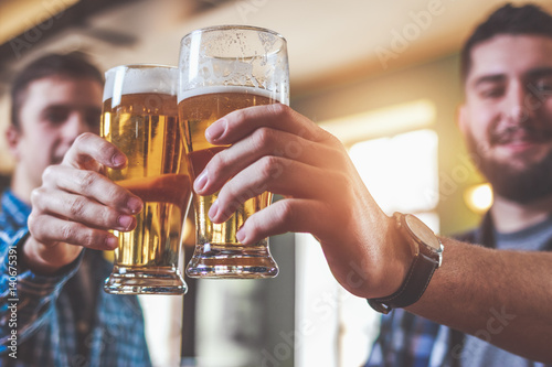 Two hipster friends clinking glasses of beer at bar photo