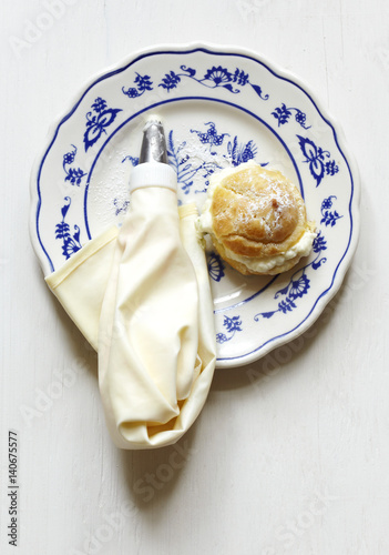Mini cream puff and piping bag on a plate.