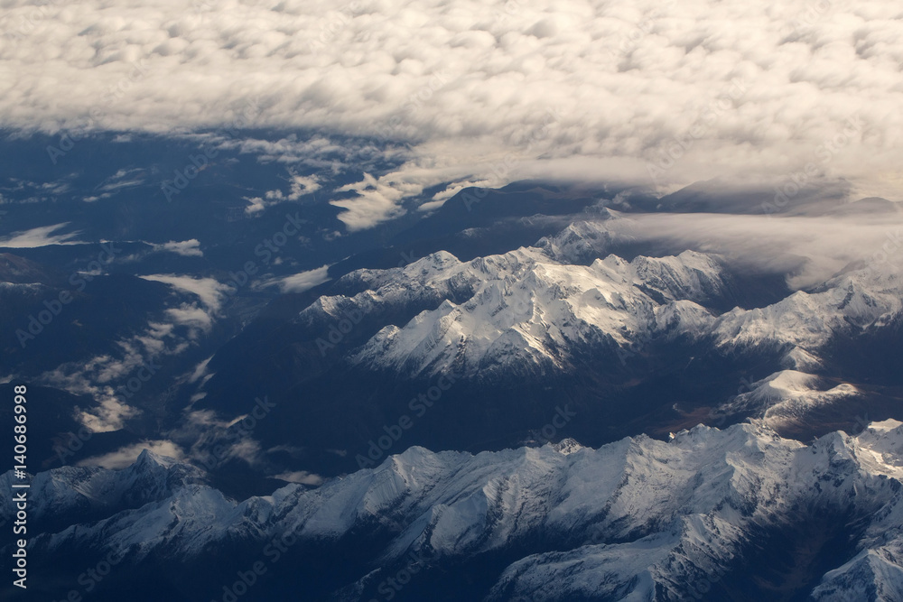 Fototapeta premium Idyllic snowy mountain peaks under clouds from plane