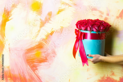 Beautiful red roses in box in hands on colorful abstract