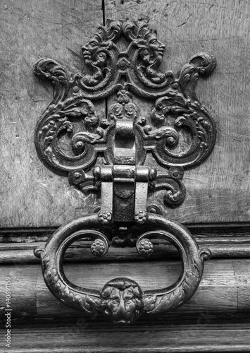 Royal style doorknocker with lion head on wooden door. Black and white.