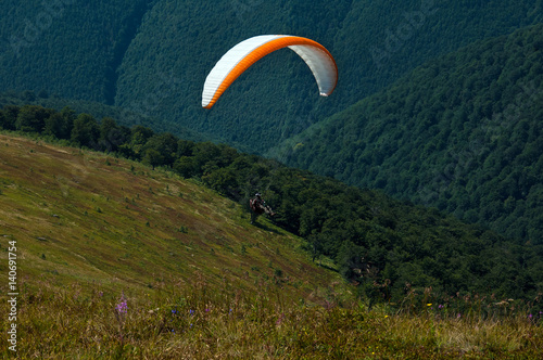Paragliding in the sky. Paraglider fly over the tops of the mountains in summer sunny day. Carpathians, Ukraine.