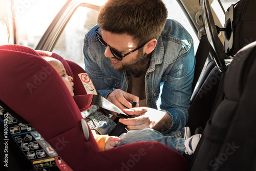 Father fasten his baby in car seat