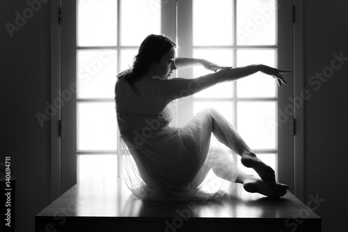 Middle aged caucasian woman in pink translucent dress poses on a table while backlit