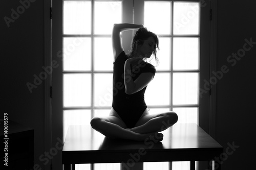 Middle aged caucasian woman in black leotard poses on a table while backlit