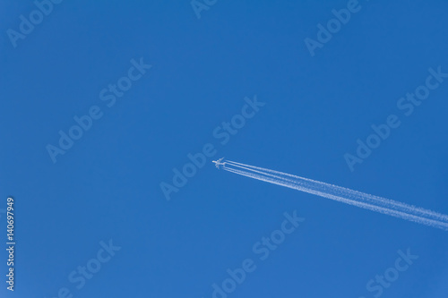 Airplane with contrails in clear blue sky